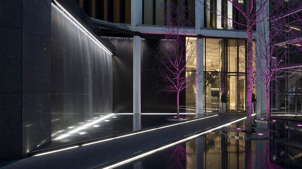 Entrance water court at night - water wall, lit paving lines and colour-lit trees