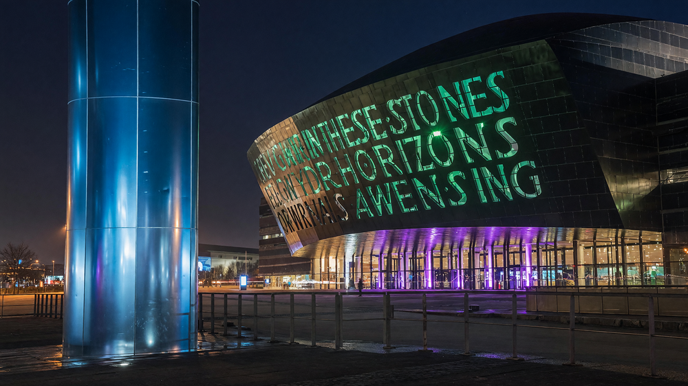 Facade at night - illuminated inscription, colour-washed colonnade and glass tower