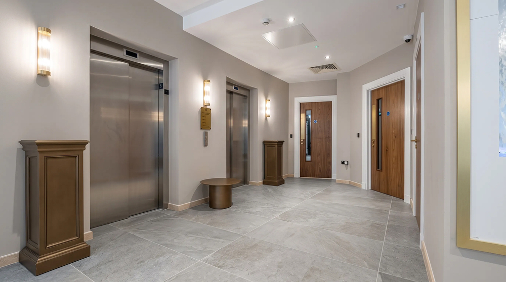 Lift lobby - paired wall sconces, stone floor and timber doors